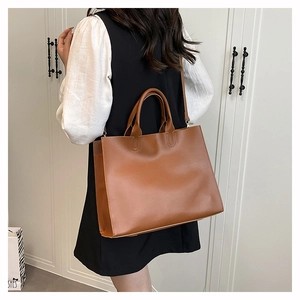 Close-up of a large brown leather tote bag with double handles and long shoulder strap