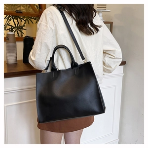 Detail of a black matte leather tote bag with sturdy handles and adjustable strap