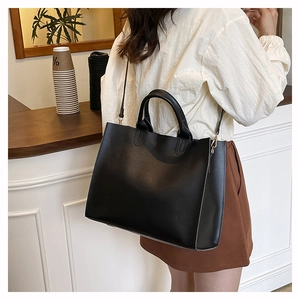 Detail of a large black leather tote bag worn by a model in a modern cafe setting