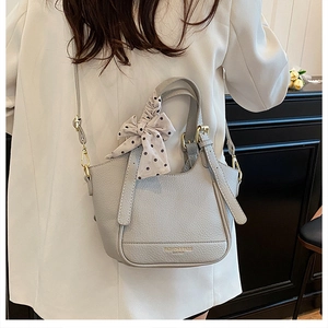 Détail du sac seau gris en cuir avec ruban à pois sur un blazer blanc élégant