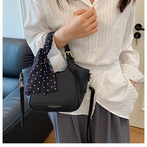 Détail du sac seau en cuir noir avec foulard à pois sur la poignée et détails dorés