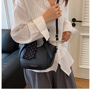 Détail du sac seau noir en cuir grainé avec logo doré et décoration de foulard à pois chic