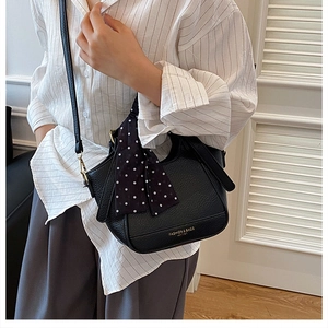 Détail du sac à main en cuir grainé noir avec foulard à pois et finitions métalliques dorées