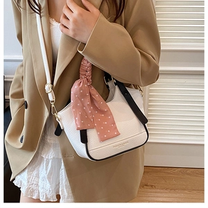 Détail d'un sac seau en cuir blanc avec foulard en soie et finitions dorées sur mannequin