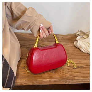 Close-up of a red patent leather box bag with unique gold handle and chain strap on a table