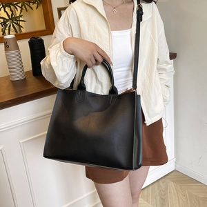 Black large capacity tote bag with adjustable shoulder strap shown in minimalist cafe setting