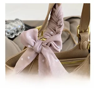 Détail du foulard en soie rose à pois noué sur la poignée d'un sac en cuir beige