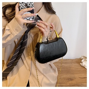 Detail of black glossy box bag with gold sculptural handle and slim chain strap