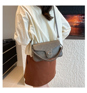 Close-up of a grey leather crossbody bag with checkered texture and silver C-shaped buckle