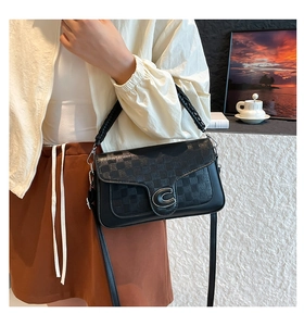 Close-up of black leather crossbody bag featuring a metal C-buckle and diamond pattern
