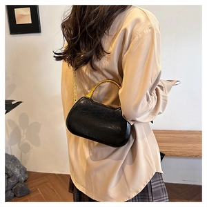 Detail of a vintage-style black cracked leather bag with a gold bamboo handle