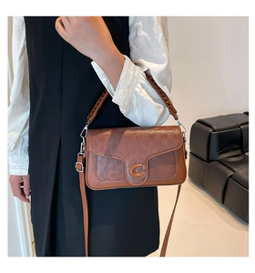 Detail of a brown leather bag showing the woven pattern cover and C-shaped metal buckle