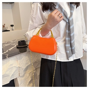 Detail of vibrant orange box bag with golden bamboo handle and chain strap on marble surface