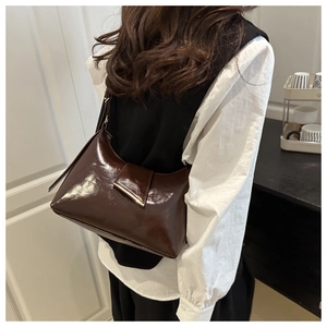 Model view of a dark brown glossy underarm bag with a gold triangular metal buckle