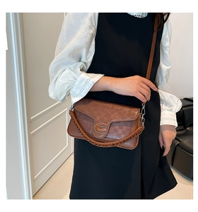 Detail of a brown plaid crossbody bag with silver C buckle and woven top handle strap