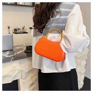 Detail of orange handbag with golden bamboo-style metal handle and elegant chain strap