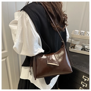 Detail view of glossy brown underarm bag with gold metal buckle on female model shoulder