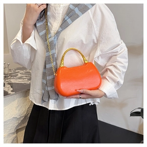 Close-up of orange structured box bag with gold bamboo handle and detachable chain