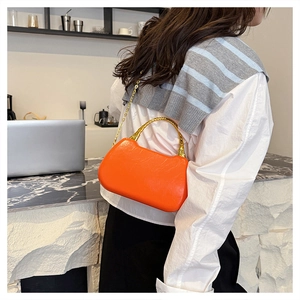 Detail of vibrant orange leather crossbody bag with iconic gold bamboo handle and chain