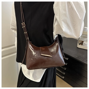 Close-up of a dark brown glossy oil wax leather underarm bag with gold metal buckle detail