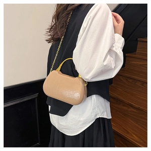 Detail of khaki patent leather box bag with gold curved handle and chain on wooden stairs