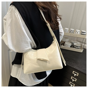 Detail of cream shoulder bag featuring gold curved metal trim and elegant flap closure