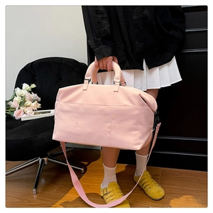 Pink duffel bag with wide shoulder strap and front pockets in a modern interior setting