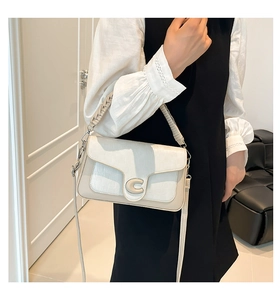 Detail of cream saddle bag featuring crocodile texture and golden C-shaped buckle