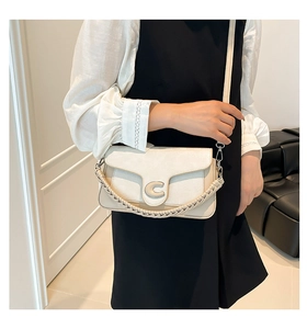 Detail of a beige trapezoid bag with silver C-buckle and woven handle on a model