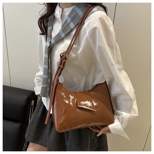 Close-up of brown glossy leather shoulder bag with adjustable strap and metal buckle