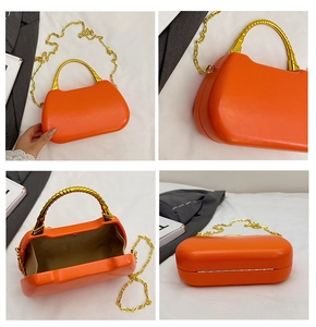 Detail of orange hardshell handbag featuring vintage gold bamboo style handle and chain strap