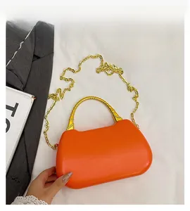 Detail view of bright orange box bag with golden bamboo handle and metal chain strap