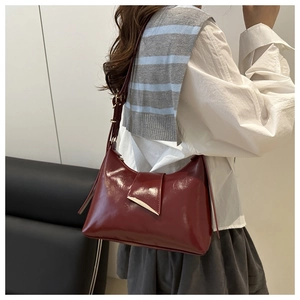 Detail of dark red glossy leather saddle bag with gold metal buckle on a shoulder