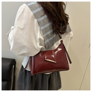 Detail of burgundy patent leather shoulder bag with a sleek gold metallic clasp
