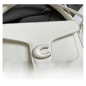 Close-up of white woven shoulder bag with a metallic C-shaped buckle and textured strap