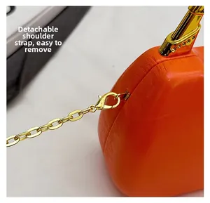 Detail of orange leather box bag showing detachable gold chain strap and bamboo metal handle