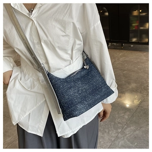 Close-up of denim shoulder bag featuring silver strap and heart-shaped metal zipper pull
