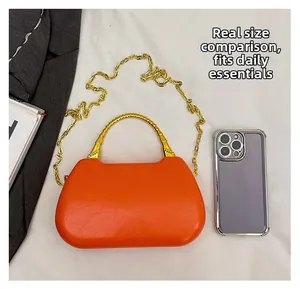 Orange box bag with gold bamboo handle and chain shown next to a phone for size comparison
