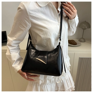 Detail of a black faux leather shoulder bag with a gold crescent buckle on the flap cover