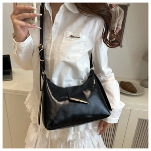 Detail of glossy black shoulder bag featuring adjustable strap and crescent gold buckle