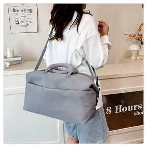 Gray travel duffel bag with dual handles and adjustable strap shown on model's shoulder