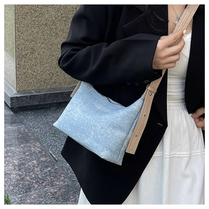 Detail of light blue denim shoulder bag featuring adjustable beige leather strap