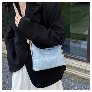 Detail shot of light blue textured denim crescent bag with a beige shoulder strap on model