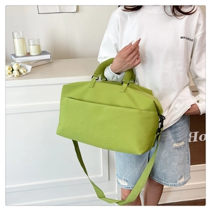 Model wearing a green waterproof travel duffel bag with a crossbody strap in a modern setting