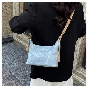 Detail of light blue denim crossbody bag with tan leather strap on a black blazer