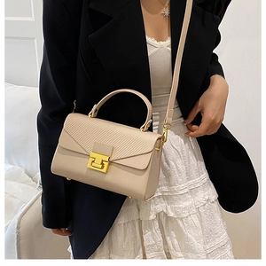 Dettaglio borsa beige con trama intrecciata e chiusura a T dorata indossata con blazer