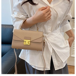 Dettaglio della borsa beige con patta testurizzata e chiusura dorata indossata dal modello