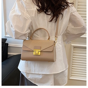 Elegante borsa a tracolla in pelle beige con fibbia a T indossata su una camicia bianca