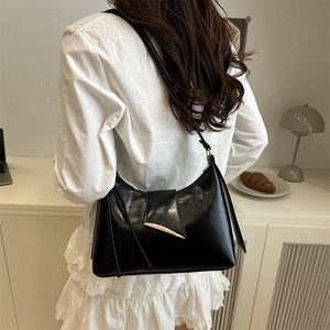 Glossy black underarm bag with gold metal buckle shown in a stylish lifestyle setting