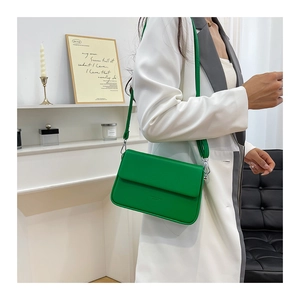 Sac à bandoulière chic en cuir PU vert porté avec un blazer blanc dans un décor moderne